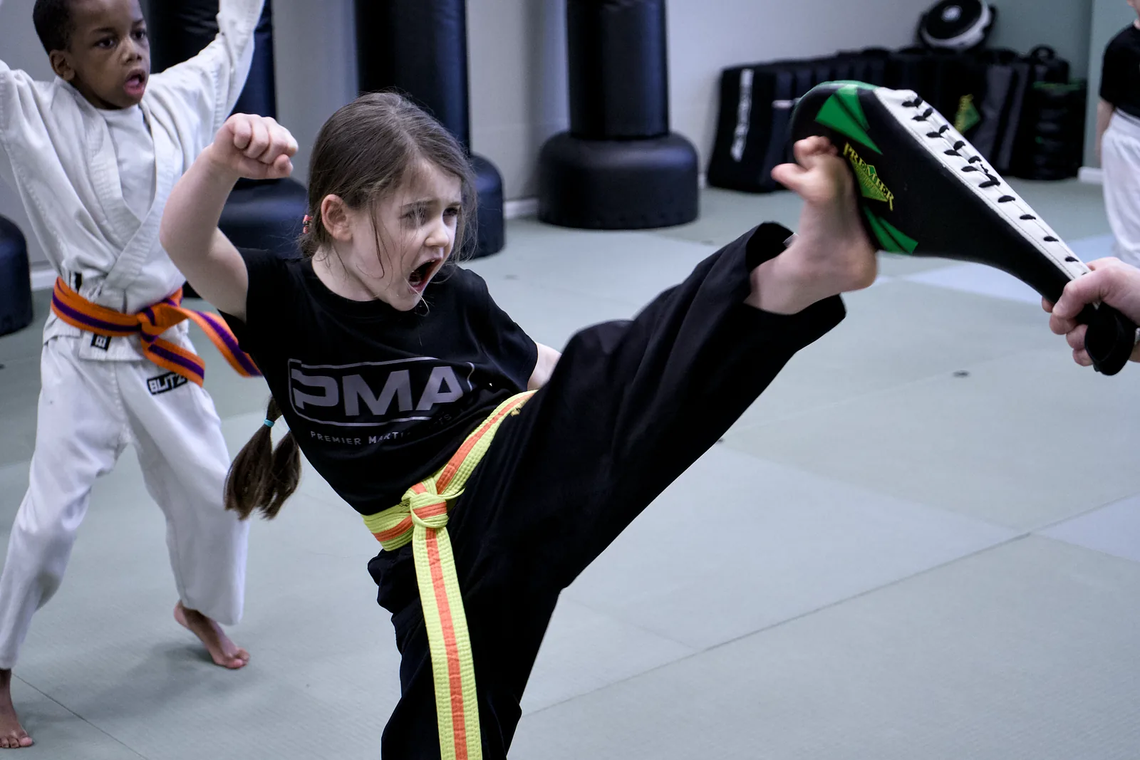 A girl in a yellow belt landing a high kick on a pad