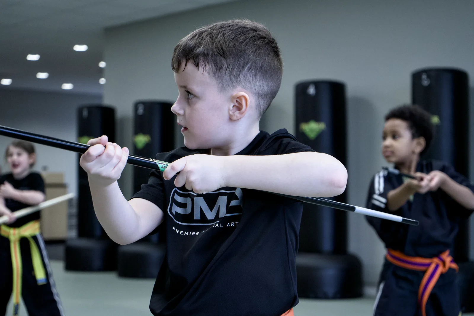 A boy in a PMA shirt holding a training staff, watching his partner